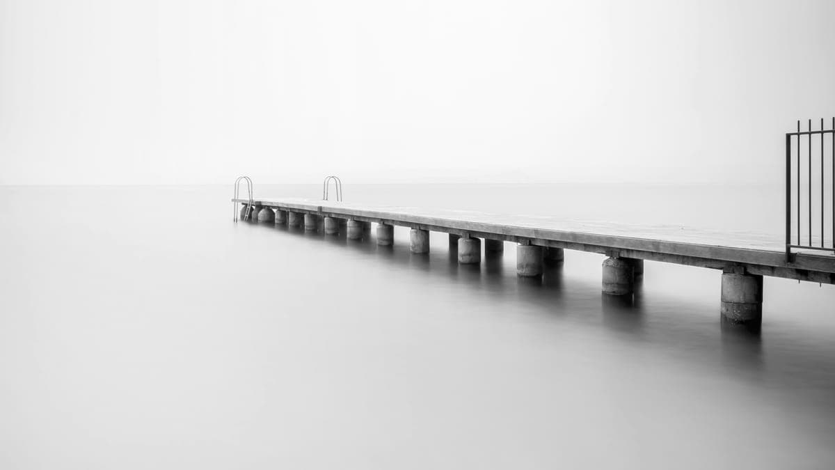 A jetty on round concrete piers running out across still, pale water to two swim ladders